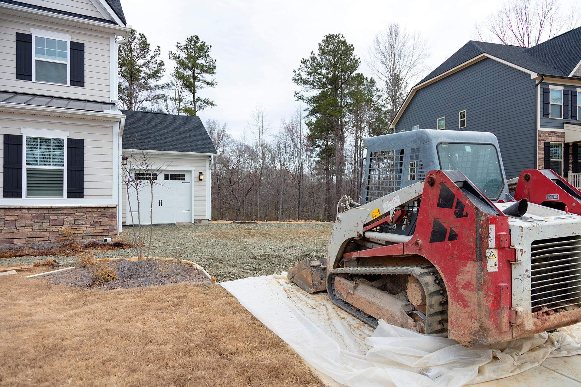 Skid steer on white covering in front of houses; construction site.
