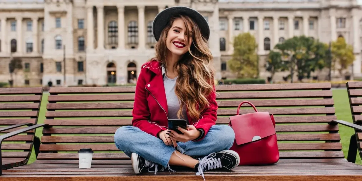 A woman is sitting on a bench with her legs crossed and holding a cell phone.