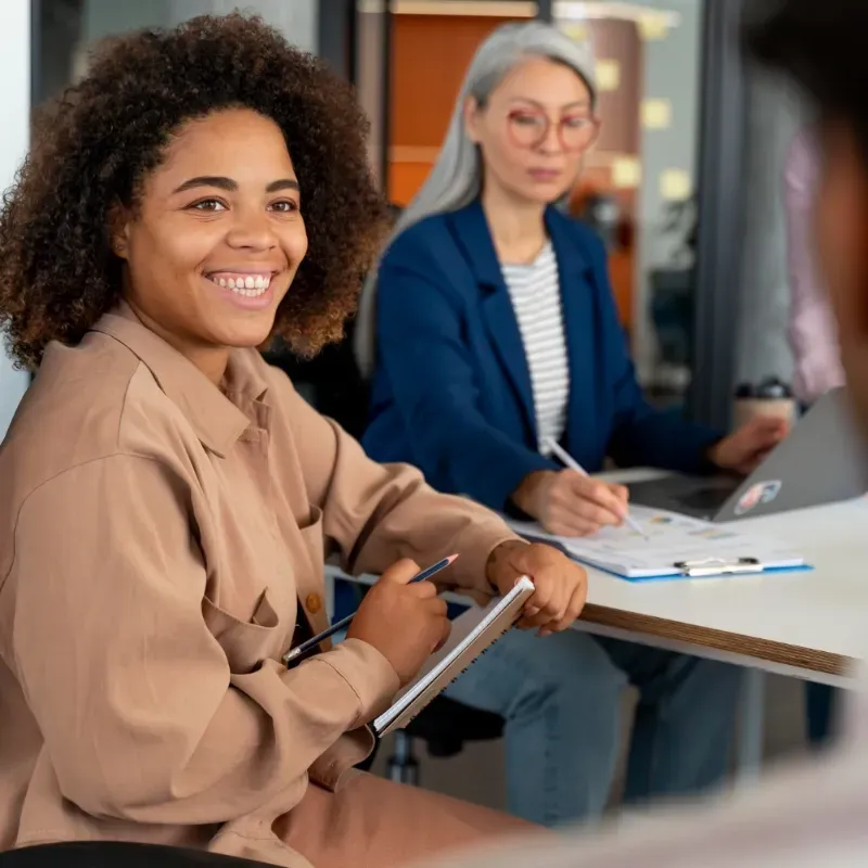 A woman is smiling while sitting at a table with other people.