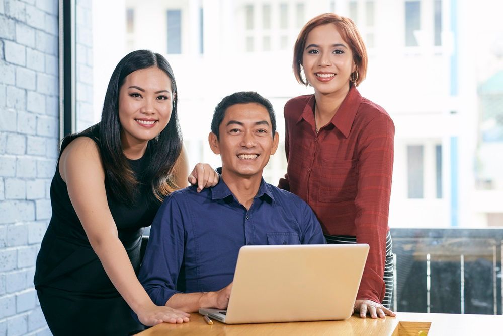 A man and two women are sitting at a table with a laptop.