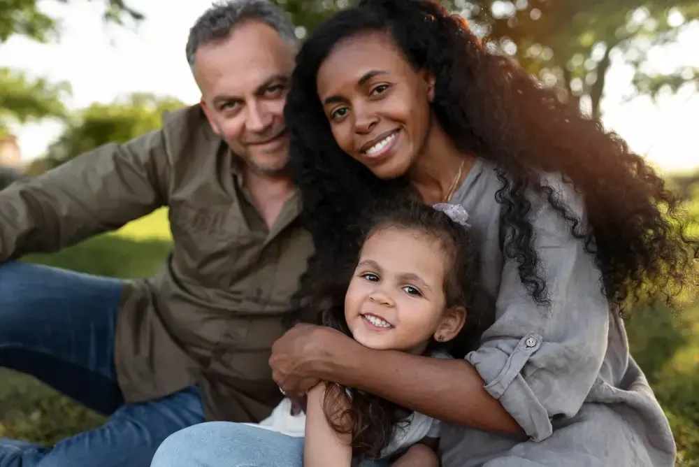 A man and woman are sitting on the grass with a little girl.