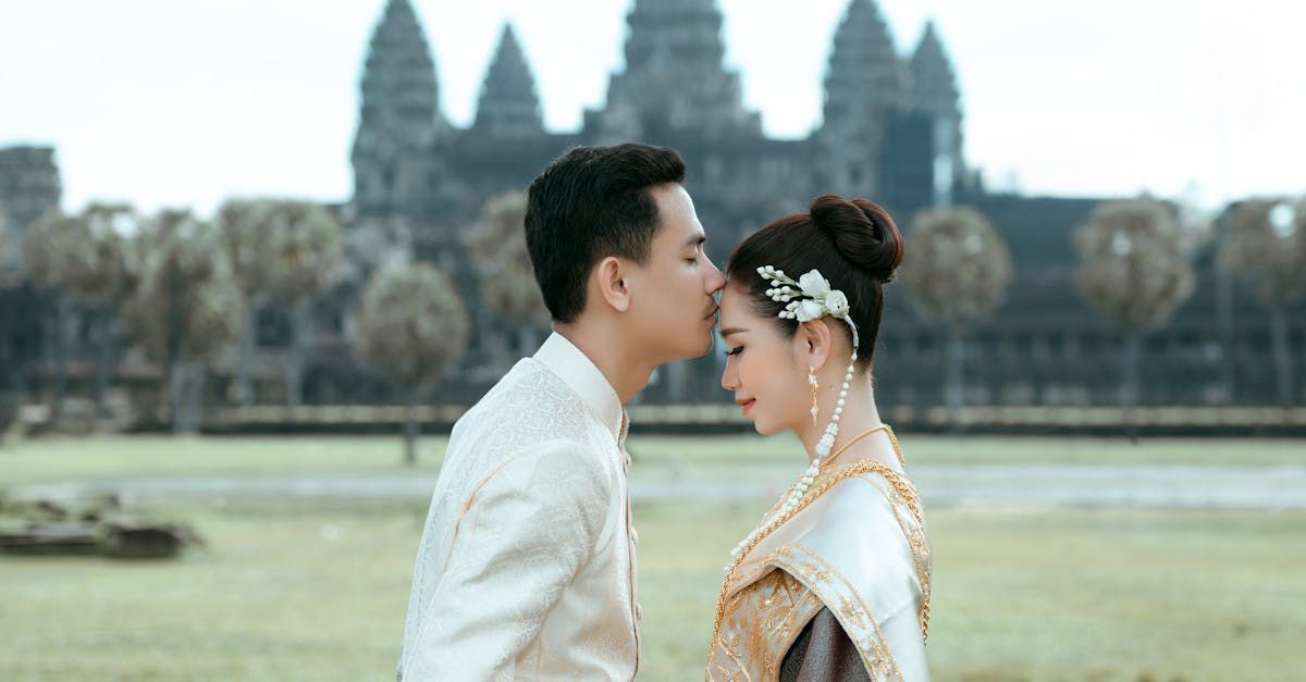 A bride and groom are kissing in front of a temple.