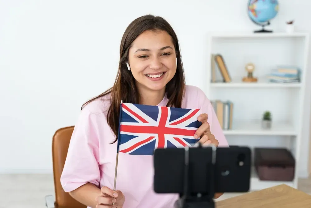 A woman is holding a british flag in front of a cell phone.