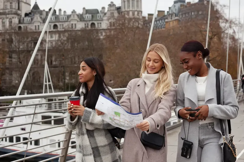 Three women are standing on a bridge looking at a map.