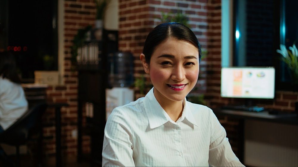 A woman is smiling while sitting at a desk in front of a computer.