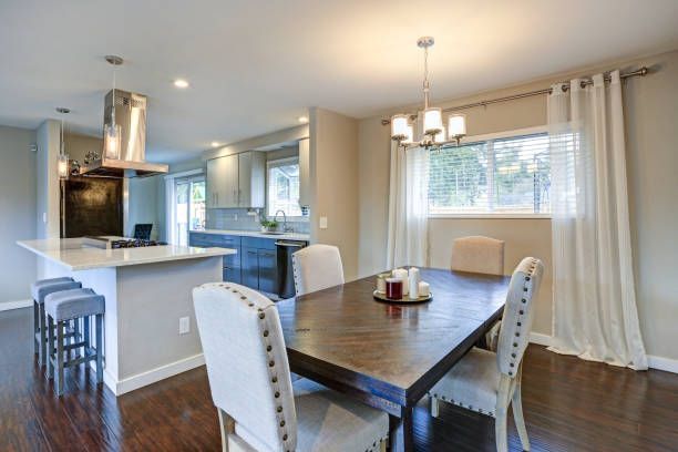A dining room with a table and chairs and a kitchen in the background.