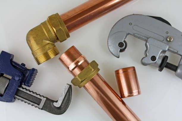 Copper pipes and wrenches are laying on a white surface.