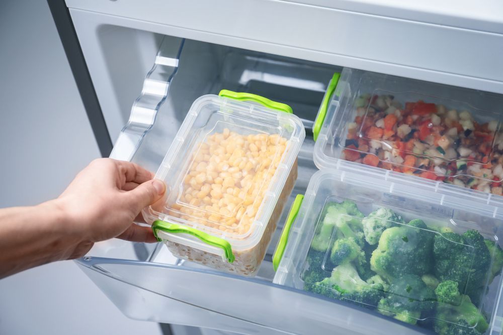 Hand Placing A Container Of Yellow Food Into A Freezer Drawer — Ace Fridge Door Seals in Mareeba, QLD