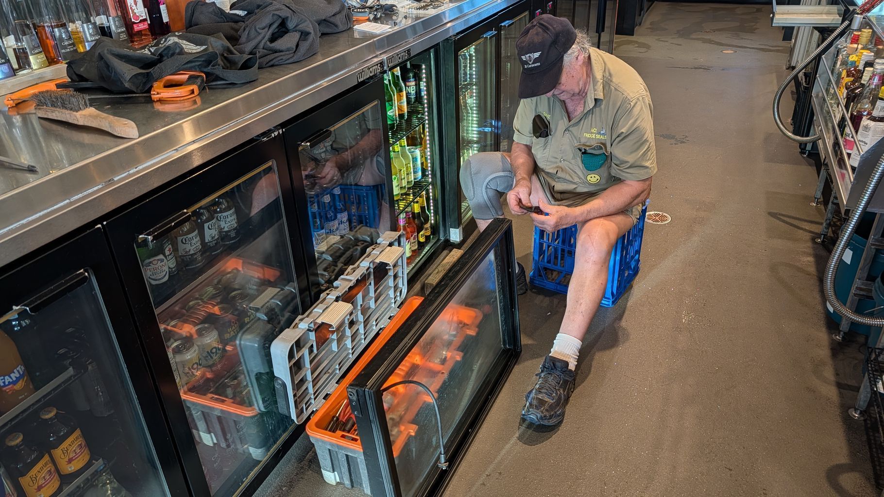 Man Sitting on the Floor in a Store Aisle Beside Glass Display Cases — Ace Fridge Door Seals In Cairns, QLD