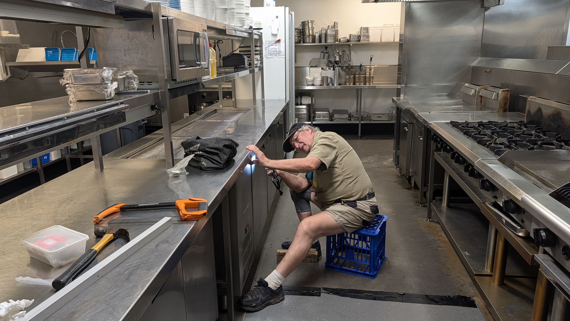 Worker Crouches in a Stainless-steel Kitchen — Ace Fridge Door Seals In Cairns, QLD