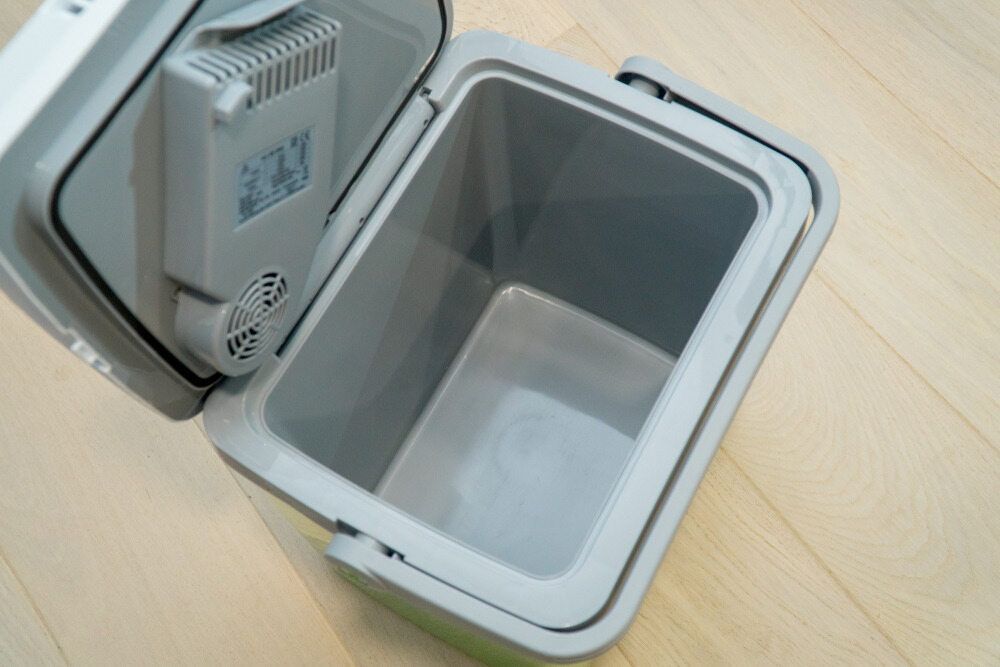 An Empty Cooler With The Lid Open Is Sitting On A Wooden Floor — Ace Fridge Door Seals In Cairns, QLD