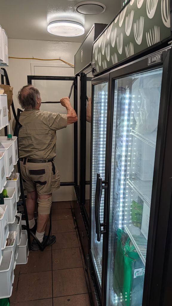 Person Reaching Up to Adjust a Ceiling Light in a Narrow Utility Room With a Refrigerator — Ace Fridge Door Seals In Cairns, QLD