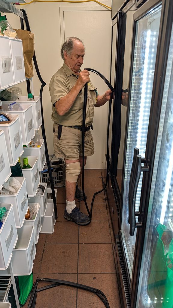 Man Using a Vacuum Cleaner in a Narrow Storage Room Beside Shelves and a Refrigerator — Ace Fridge Door Seals In Cairns, QLD