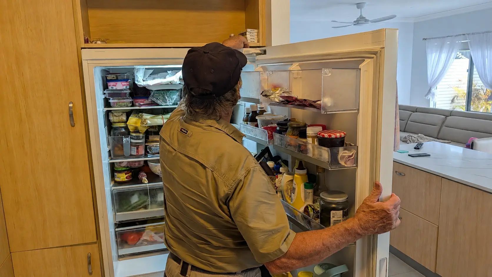Person Opening an Empty Refrigerator in a Kitchen, With the Freezer Door Held Open — Ace Fridge Door Seals In Cairns, QLD