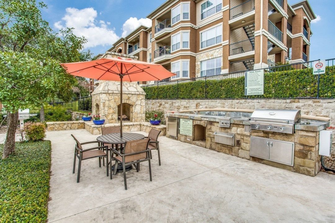 Outdoor patio with seating, grill station, and fireplace, backed by apartment building.