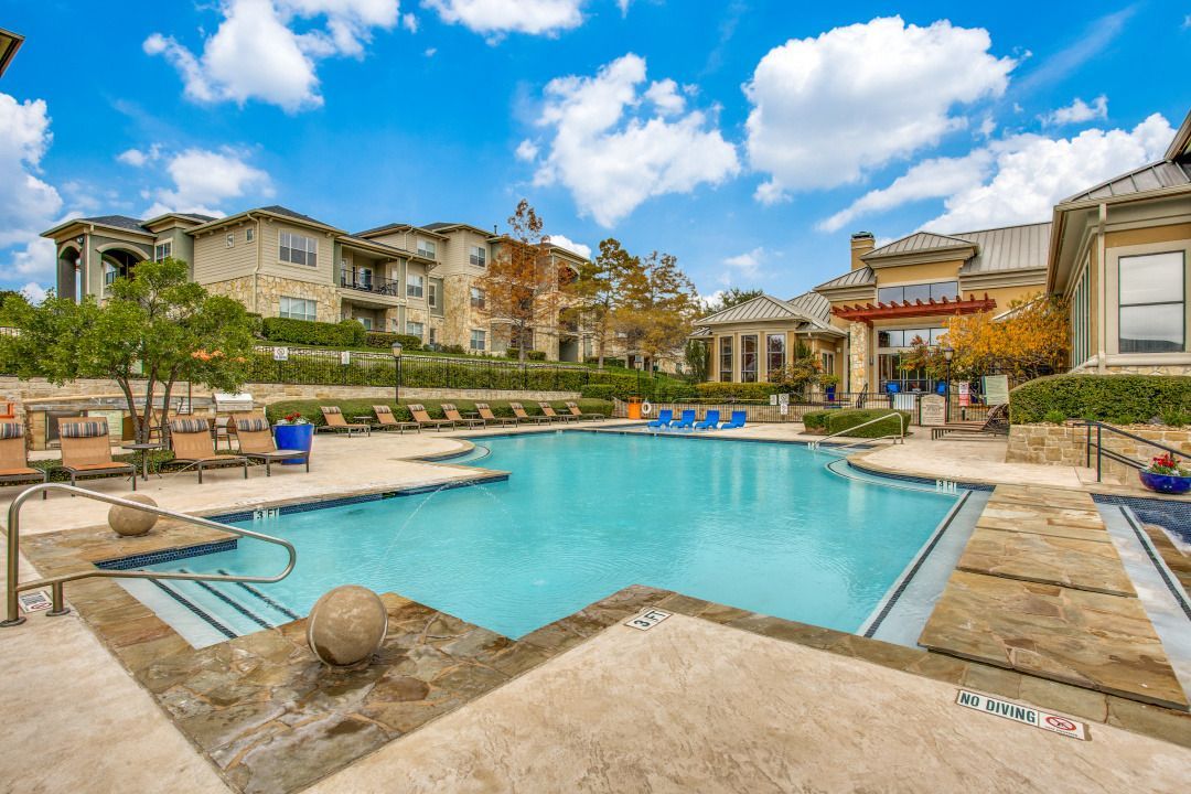 Outdoor pool at a multifamily community with surrounding lounge chairs and clubhouse.