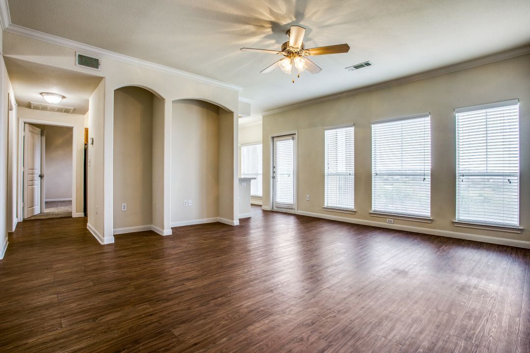 Spacious living room with wood-look flooring, multiple windows, and a ceiling fan.