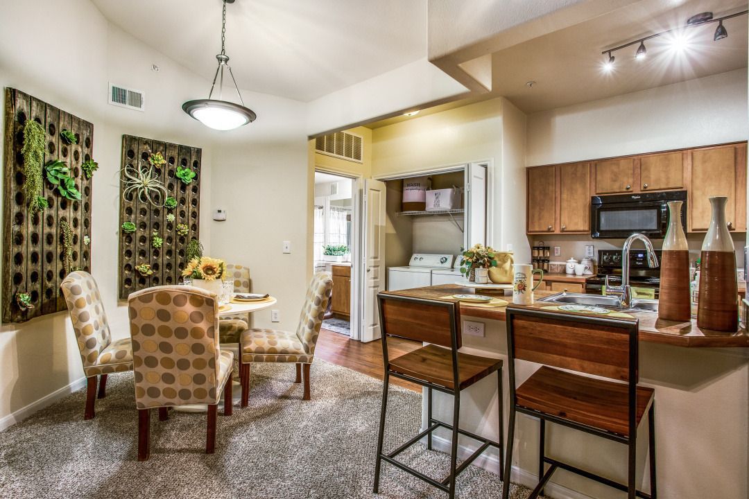 Interior of an apartment: dining area with patterned chairs, kitchen island, and laundry closet.