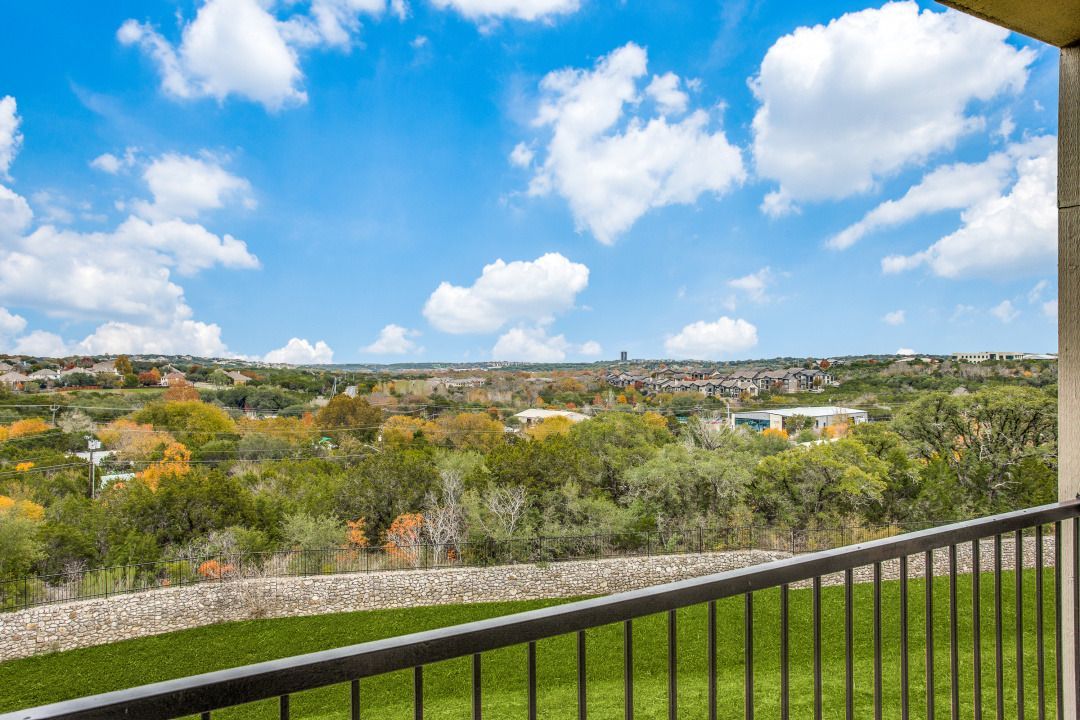 Balcony railing overlooking a green lawn, trees, and distant houses.