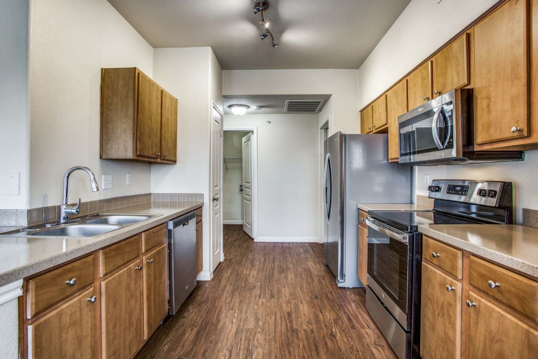 Galley-style apartment kitchen with wood cabinets, stainless steel appliances, and laminate flooring.