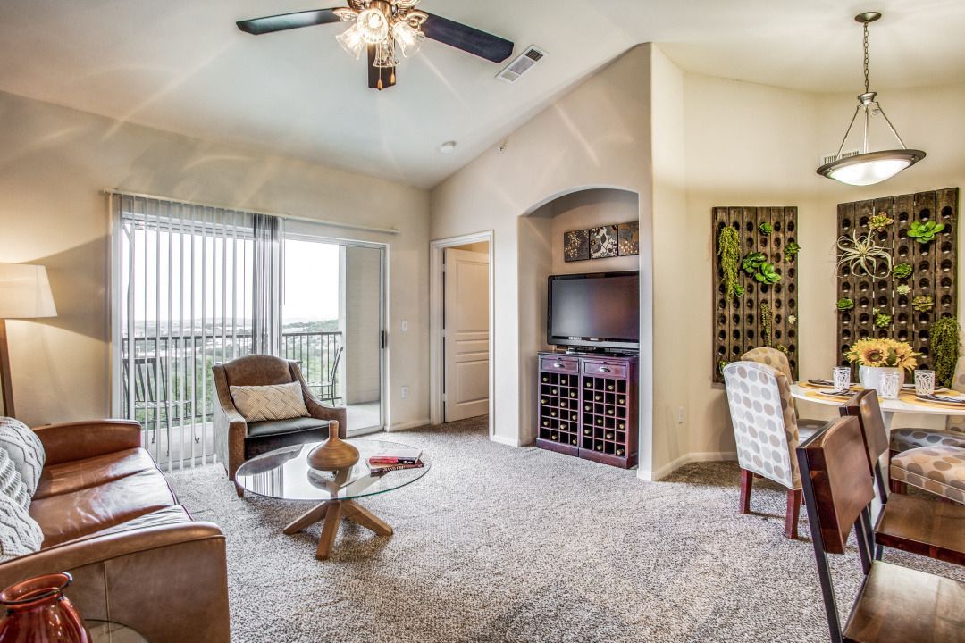 Living room with beige walls, carpet, sofa, chairs, glass coffee table, TV, and balcony door.