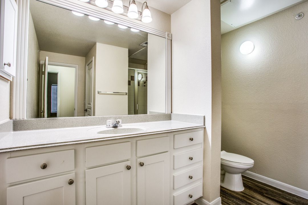 White bathroom vanity with sink, large mirror, and toilet.