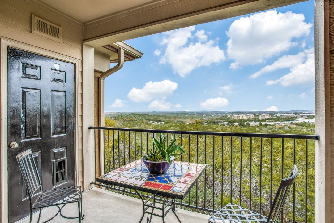 Balcony with a tiled table, two metal chairs, a plant, and a distant landscape view.