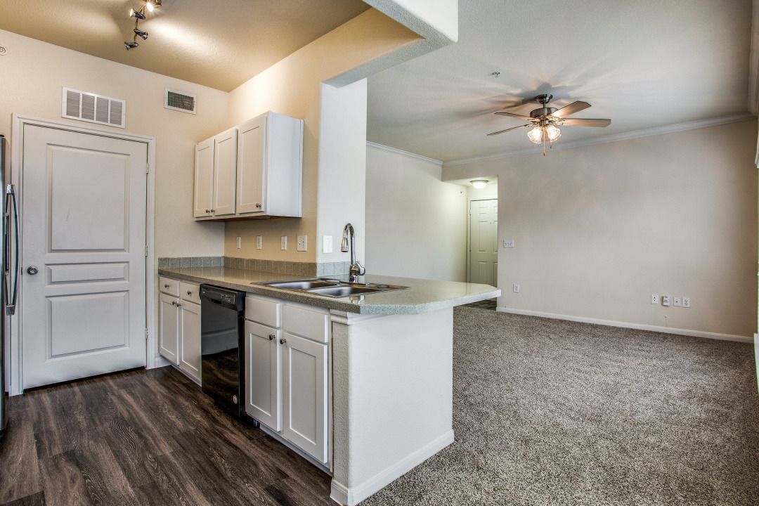 Kitchen with white cabinets, dark wood-look floor, and light gray countertops, open to a living area with beige carpet.