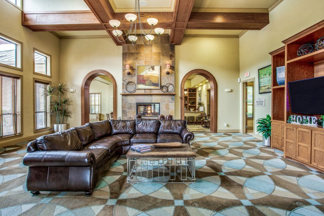 Spacious community lobby with a large brown leather sectional, a stone fireplace, and arched doorways.