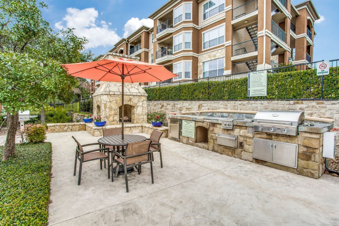 Outdoor community grilling area with a stone fireplace, built-in grills, and seating.