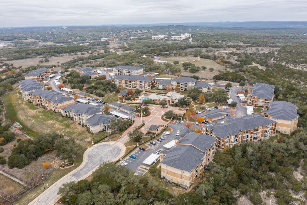 Aerial view of a large apartment community with multiple buildings, roads, and a central courtyard with a pool.