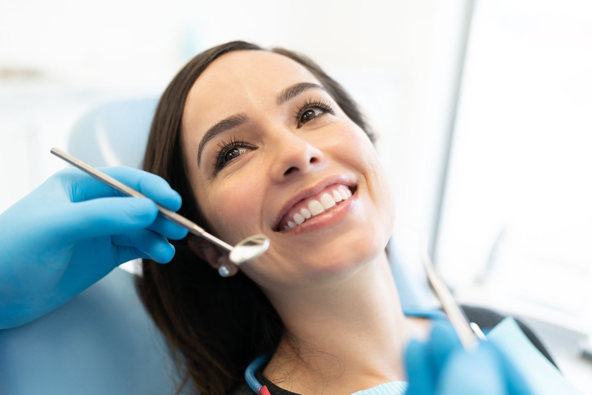 Un paziente seduto sulla poltrona odontoiatrica sorride mentre il dentista tiene in mano uno specchietto e uno strumento odontoiatrico.