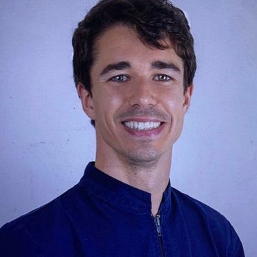 Una persona con i capelli scuri e un sorriso lieve indossa una felpa blu scuro con cerniera, su uno sfondo azzurro.