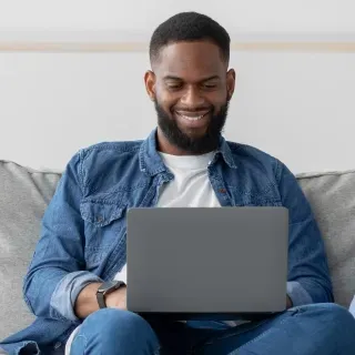 A man is sitting on a couch using a laptop computer.