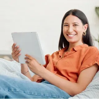 A woman is sitting on a bed holding a tablet computer.