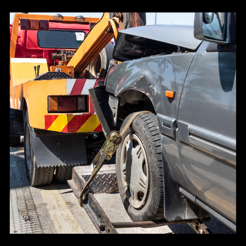 Damaged gray car being towed by a yellow and red tow truck.