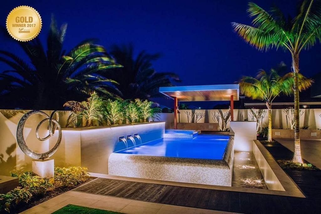 Nighttime shot of a lit pool with landscaping, including palm trees and a sculpture.
