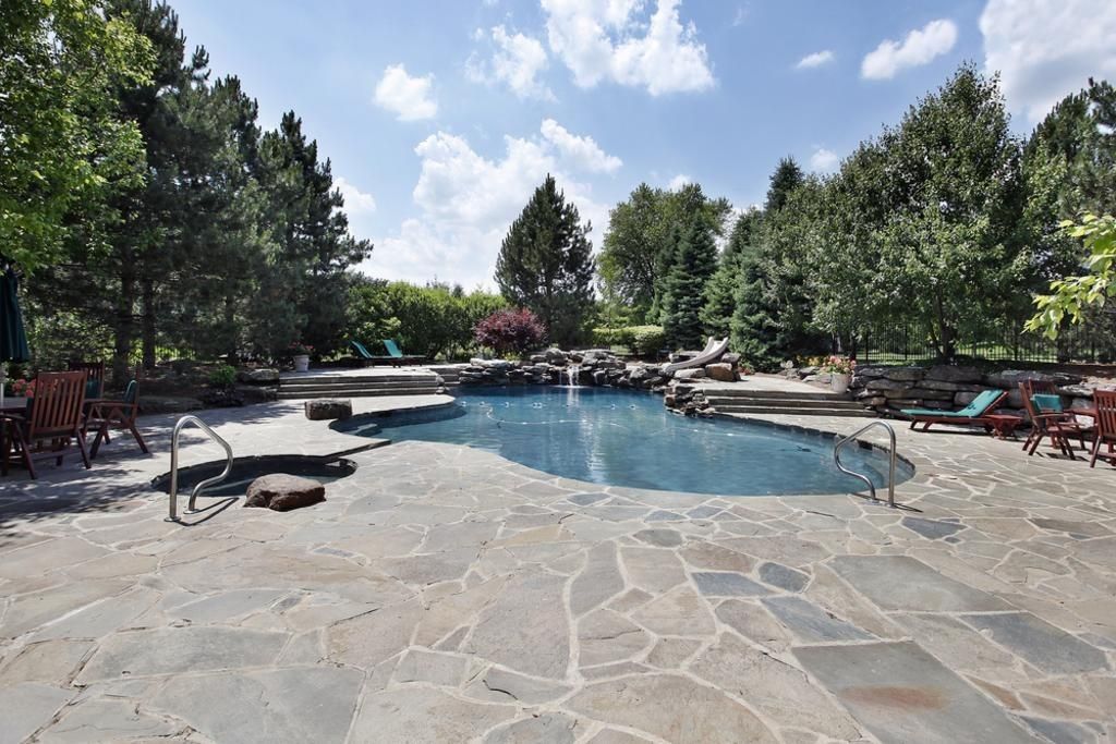 Backyard pool with stone patio, trees, and blue sky with clouds.