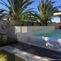 Pool with palm trees, white wall, and stone border, on a sunny day.