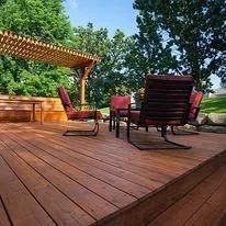 Wooden deck with chairs and pergola in a backyard setting.