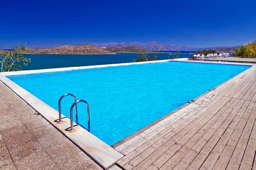 Swimming pool with blue water and water view. Wooden deck, blue sky and mountains in the distance.