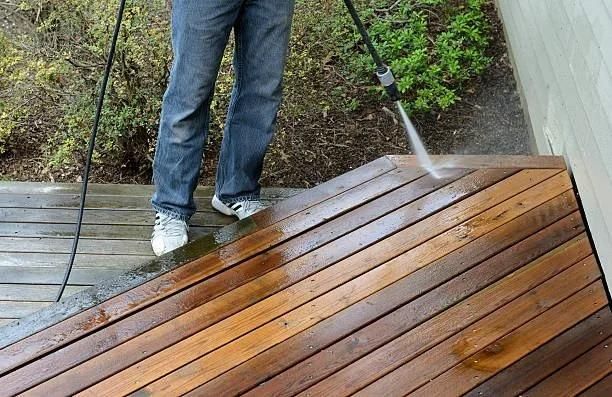 Person power washing a wooden deck with a high-pressure cleaner.