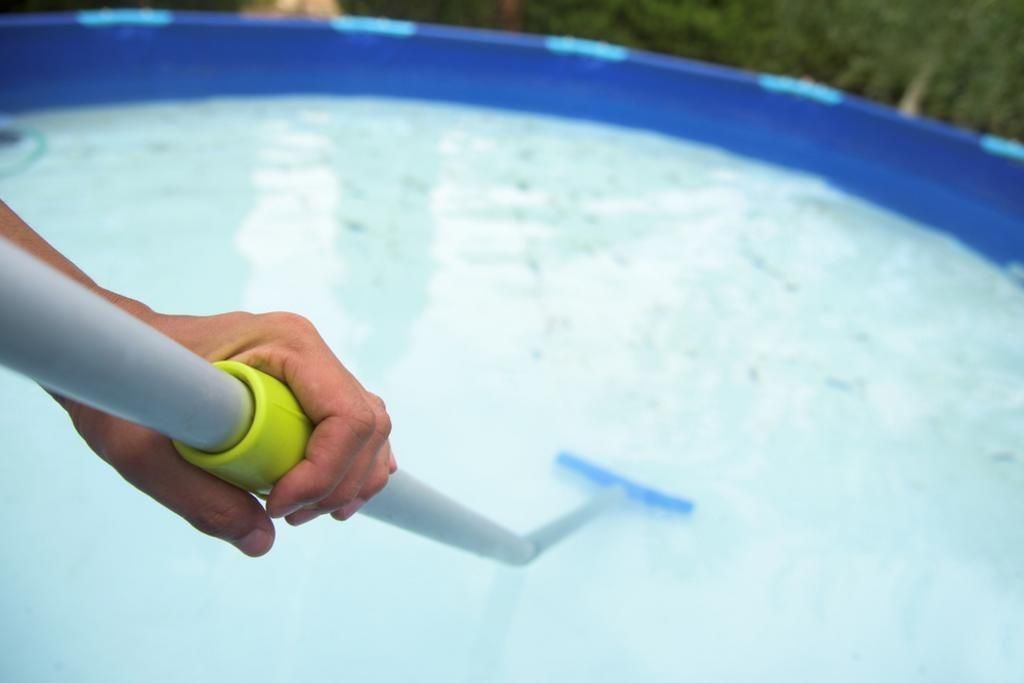 Hand holding a pool cleaning brush, cleaning a partially filled blue pool.