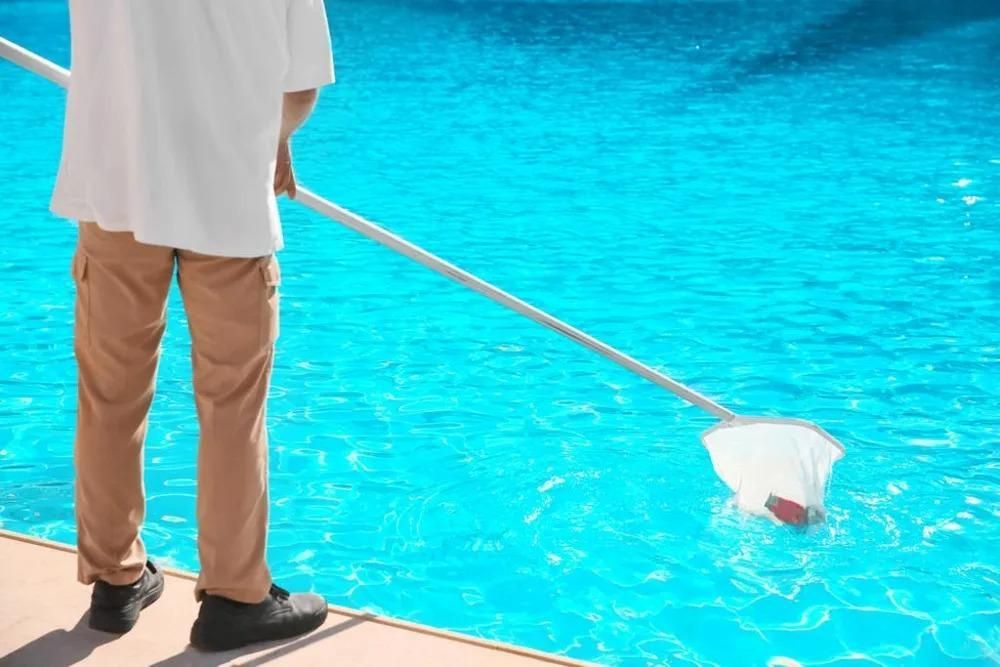 Person using a net to clean a blue swimming pool.