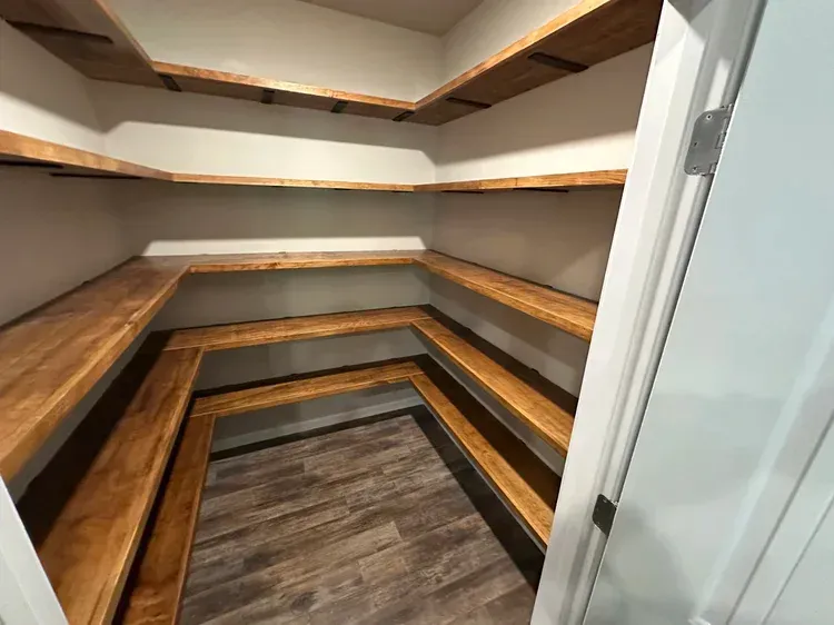 Empty pantry with wooden shelves and flooring. White walls, door frame visible.