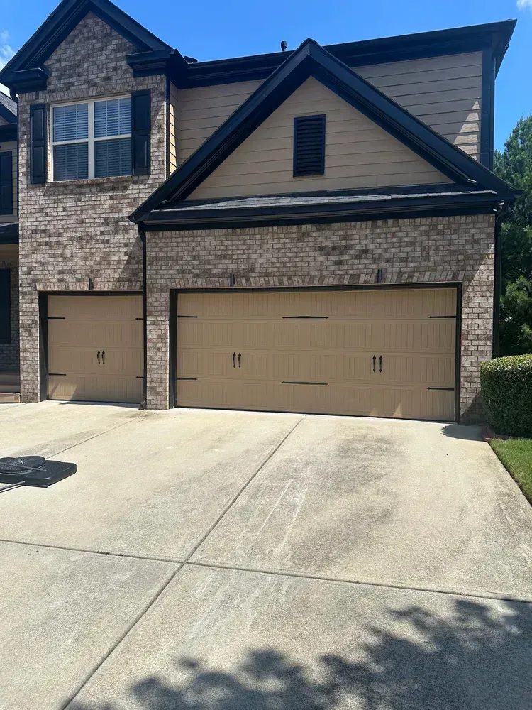Two-story house with brick and tan garage doors on a concrete driveway.