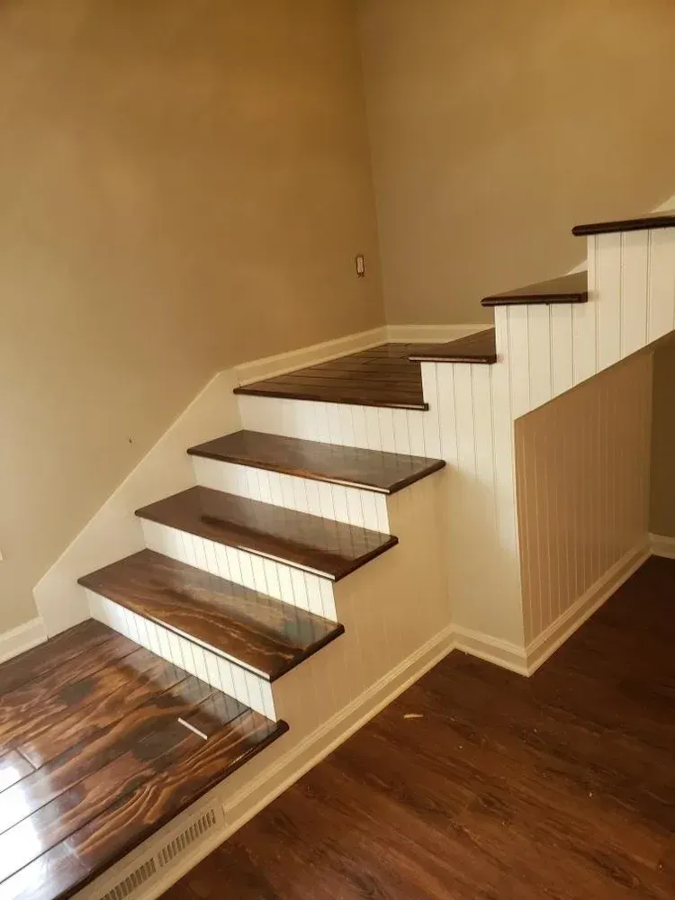 Wooden stairs with dark treads and white risers, set in a corner with wood-look flooring.
