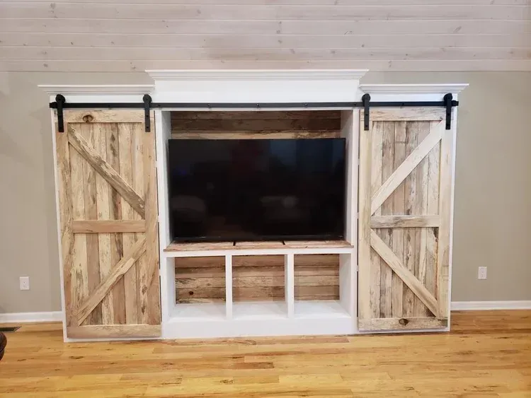 Rustic wood entertainment center with barn doors, shelving, and mounted TV.