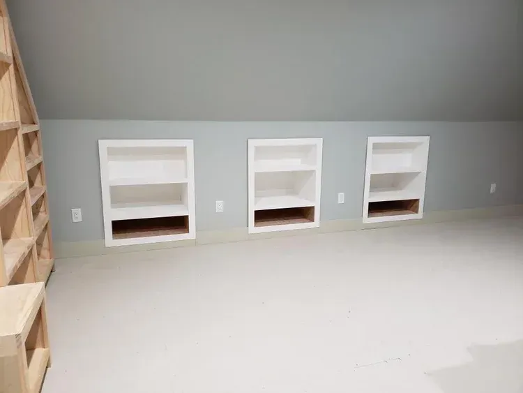 Three built-in white bookshelves on gray wall with a light beige carpeted floor.