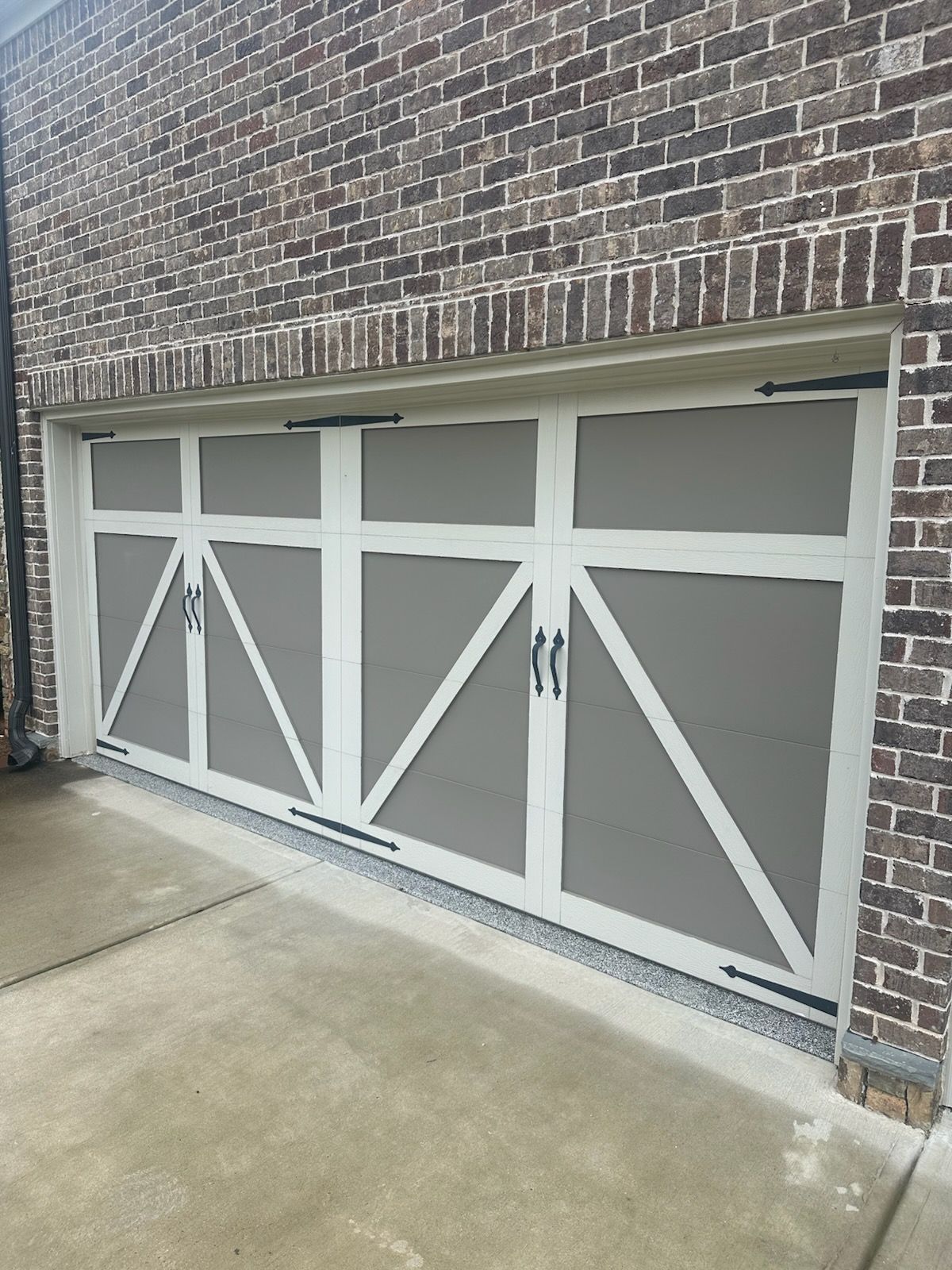 White and gray garage doors with black hardware against a brick wall.